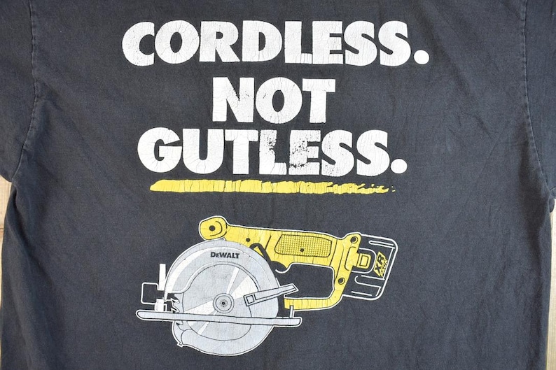 May include: Black t-shirt with white text that reads "Cordless. Not Gutless." and a yellow and black illustration of a DeWalt circular saw.