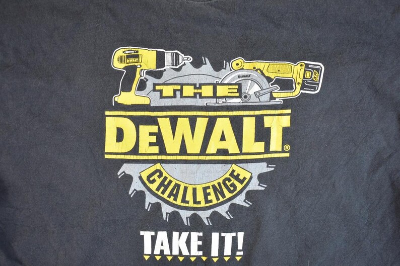 May include: Black t-shirt featuring a yellow and black graphic of a drill and circular saw with the text "The Dewalt Challenge Take It!"