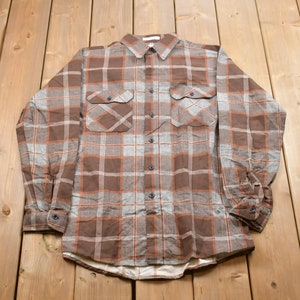 May include: A brown and gray plaid flannel shirt with long sleeves and button-up closure.