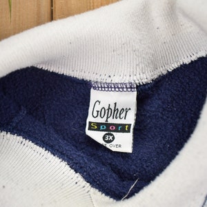 May include: A navy blue sweatshirt with white trim and a white tag that says "Gopher Sport 3X" in colorful letters.