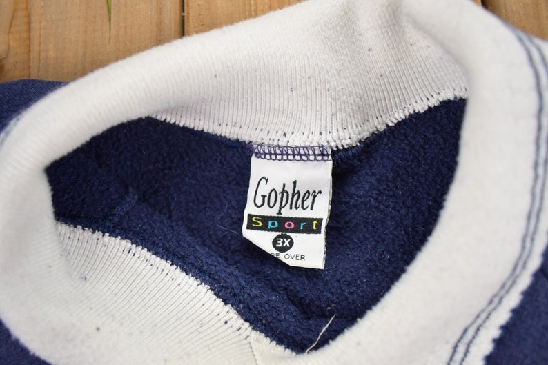 May include: A navy blue sweatshirt with white trim and a white tag that says "Gopher Sport 3X" in colorful letters.