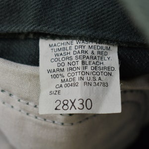 May include: A white care label with black text detailing washing instructions for a pair of jeans. The label reads "MACHINE WASH WARM, TUMBLE DRY MEDIUM, WASH DARK & RED COLORS SEPARATELY, DO NOT BLEACH, WARM IRON IF DESIRED, 100% COTTON/COTON, MADE IN U.S.A., CA 00492 RN 34783, SIZE 28X30".