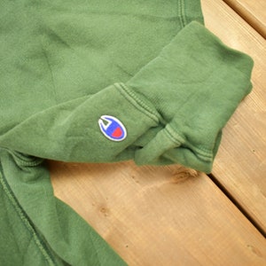 May include: Green sweatshirt with a white and black patch that says "NY" and a small blue and red Champion logo on the sleeve.