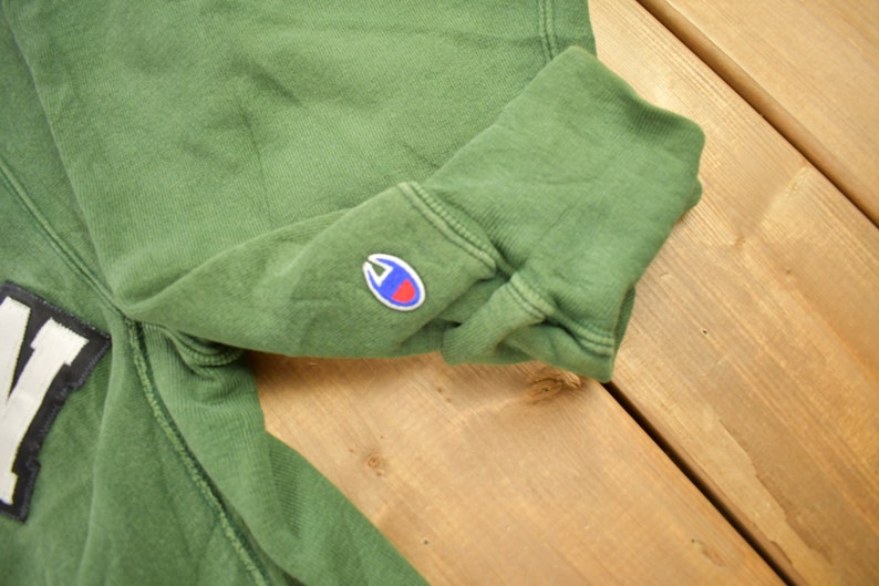 May include: Green sweatshirt with a white and black patch that says "NY" and a small blue and red Champion logo on the sleeve.