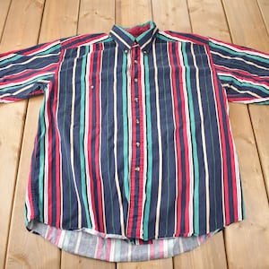 Peut inclure: Une chemise à manches courtes à boutons avec des rayures verticales rouges, vertes, jaunes et blanches sur un fond bleu marine.