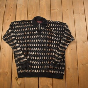 Peut inclure: Un chemisier à manches longues noir avec un motif géométrique dans des tons de brun et beige. La chemise a une fermeture éclair au col.