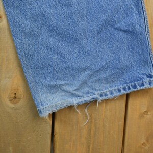 May include: A close-up of a pair of blue denim jeans with frayed edges. The jeans are laying on a wooden surface.