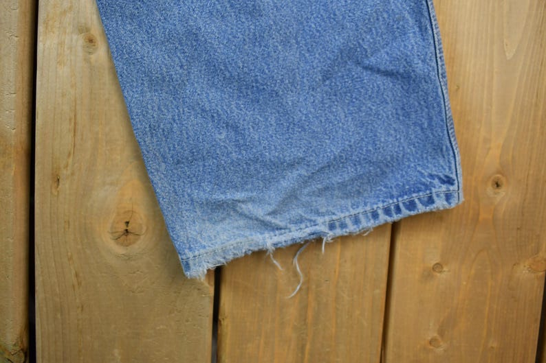 May include: A close-up of a pair of blue denim jeans with frayed edges. The jeans are laying on a wooden surface.