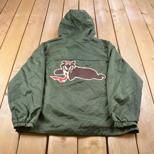May include: Green hooded jacket with a brown bear wearing a red hat and holding a red fish on the back.