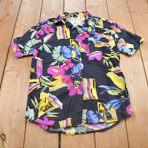 May include: A black short-sleeved button-down shirt with a colorful tropical print. The print features yellow, pink, blue, and green flowers and leaves.