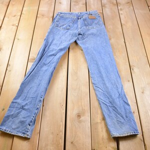 May include: A pair of light blue denim jeans laid flat on a wooden surface. The jeans have a classic straight leg style and a light wash.