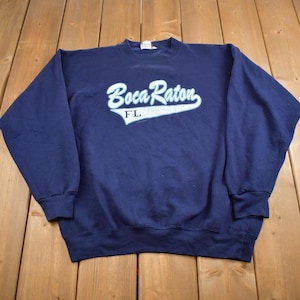 May include: A navy blue sweatshirt with a white graphic that says "Boca Raton, FL" in a vintage style font.