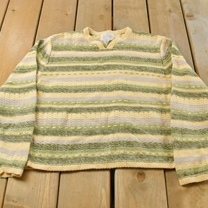 May include: A long-sleeve knit sweater featuring horizontal stripes in shades of light yellow, sage green, and cream. The garment has a textured, open-weave pattern throughout with a notched crew neckline and ribbed trim at the collar and cuffs.