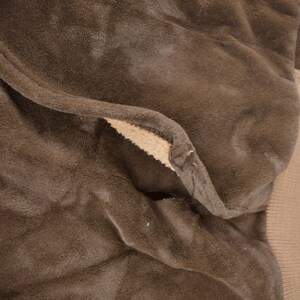 May include: Close-up of the brown fleece lining of a jacket. The fleece is soft and plush, and the seams are visible.