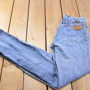 May include: A pair of light blue denim jeans with a brown leather patch on the back pocket that says "Wrangler".