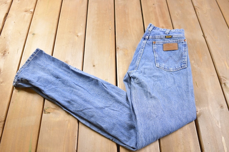 May include: A pair of light blue denim jeans with a brown leather patch on the back pocket that says "Wrangler".