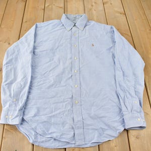 Peut inclure: Une chemise boutonnée à manches longues bleu clair avec un petit logo brodé sur la poitrine gauche.