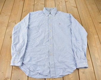 May include: A light blue long-sleeved button-down shirt with a small embroidered logo on the left chest.