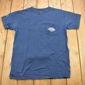以下が含まれることがあります： 左胸に小さなポケットが付いた濃い青色のTシャツ。ポケットには白いハーレーダビッドソンのロゴがあります。