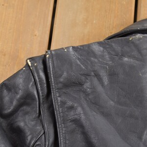 May include: Black leather jacket with a zipper closure and a collar. The jacket has a worn look with some visible wear and tear.