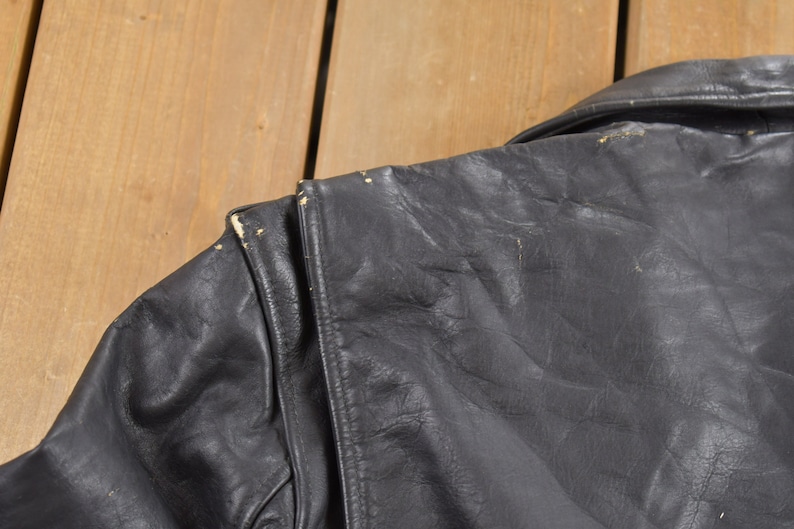 May include: Black leather jacket with a zipper closure and a collar. The jacket has a worn look with some visible wear and tear.