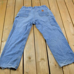 May include: A pair of light blue denim carpenter jeans with multiple pockets and a brown leather patch on the back.