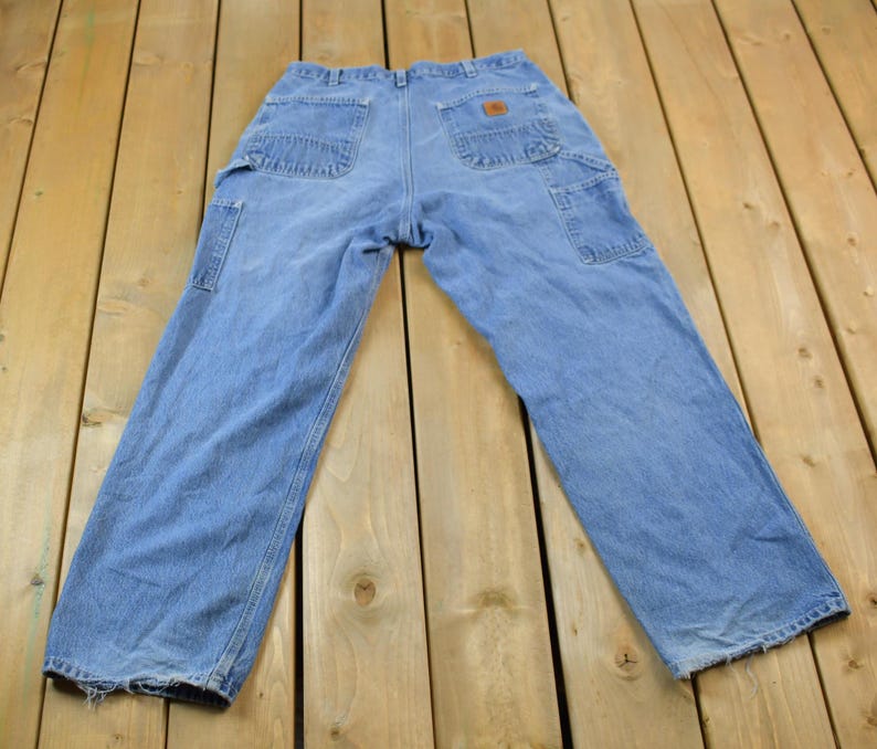 May include: A pair of light blue denim carpenter jeans with multiple pockets and a brown leather patch on the back.