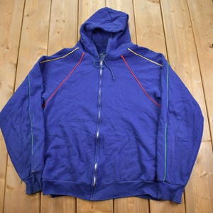 Puede incluir: Una sudadera con capucha azul con cierre de cremallera y detalles de costura coloridos alrededor del cuello y las mangas.