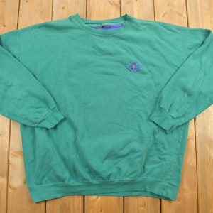May include: A green long-sleeved sweatshirt with a blue and purple embroidered logo on the front. The logo features a shield with a sunburst design and the text "Salzburg".