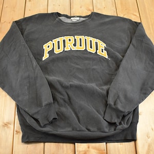 May include: A black crew neck sweatshirt featuring the word "PURDUE" in yellow and white lettering. The sweatshirt has long sleeves and is made of a soft material. The measurements are in centimetres.