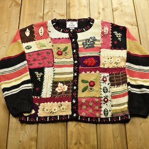 Peut inclure: Un cardigan noir en patchwork multicolore avec des fleurs et des feuilles brodées. Le cardigan a une fermeture boutonnée et est fait d'un tissu tricoté doux. L'étiquette sur le cardigan indique "Tiara".
