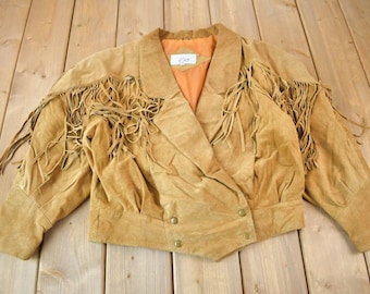 May include: A brown suede jacket with fringe detailing on the sleeves and collar. The jacket has a button closure and a double-breasted style.