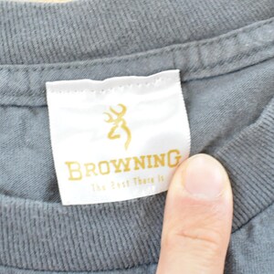 May include: Close-up of a gray t-shirt collar with a white tag. The tag features the word "BROWNING" in gold lettering, along with a gold deer logo and the text "The Best There Is".