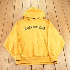 May include: A yellow hooded sweatshirt with the text "FRAMINGHAM STATE" in black across the chest. The sweatshirt has a front pocket and a drawstring hood. The garment is made of a soft material.