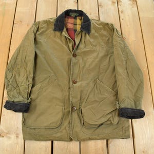 May include: Olive green jacket with a corduroy collar and plaid lining. The jacket has two large front pockets and button closures. The cuffs are black. A classic outerwear piece.