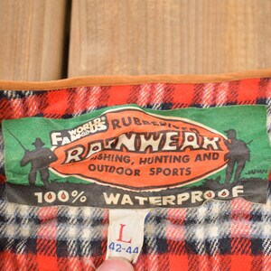 May include: A green and red plaid flannel shirt with a brown leather trim. The shirt has a label that reads "World's Famous Rubberized Rainwear Fishing, Hunting and Outdoor Sports 100% Waterproof" and a size tag that reads "L 42-44".