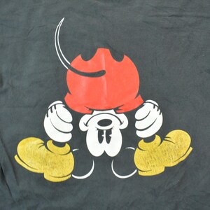 May include: Black t-shirt with a cartoon image of Mickey Mouse wearing a red hat and looking down. Mickey Mouse is wearing yellow shoes and white gloves.