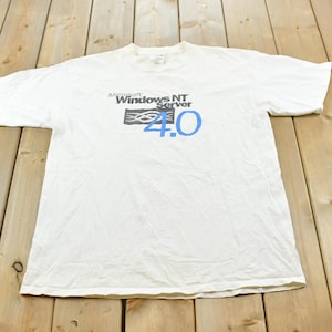 Könnte beinhalten: Ein weißes T-Shirt mit kurzen Ärmeln und einem Aufdruck auf der Brust. Der Aufdruck zeigt den Text Microsoft Windows NT Server in Schwarz, mit einem stilisierten schwarzen rechteckigen Symbol über der großen, hellblauen Zahl 4.0 darunter.
