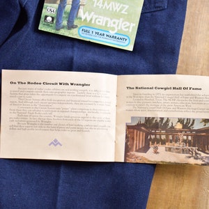 May include: A pamphlet with the text "On The Rodeo Circuit With Wrangler" and "The National Cowgirl Hall Of Fame" on a blue denim background. The pamphlet has a picture of a building with a fountain in front of it.