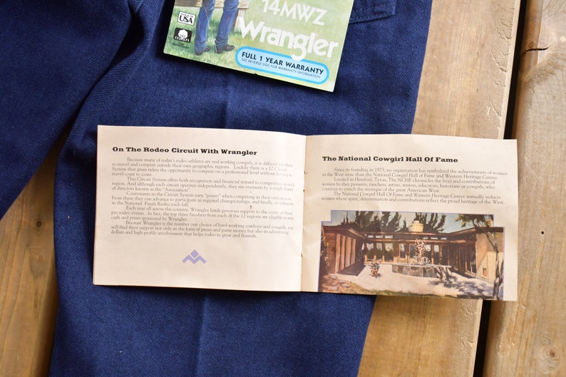 May include: A pamphlet with the text "On The Rodeo Circuit With Wrangler" and "The National Cowgirl Hall Of Fame" on a blue denim background. The pamphlet has a picture of a building with a fountain in front of it.