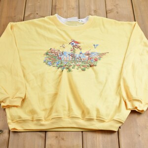 May include: A yellow sweatshirt with a colorful embroidered design of a birdhouse, flowers, and birds.