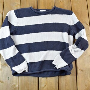 Può includere: Un maglione a righe con strisce orizzontali bianche e blu navy. Il maglione è realizzato in un tessuto morbido e lavorato a maglia.