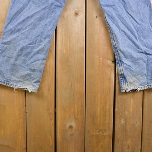 May include: A pair of light blue denim jeans hanging on a wooden fence. The jeans have a faded look and are slightly distressed.