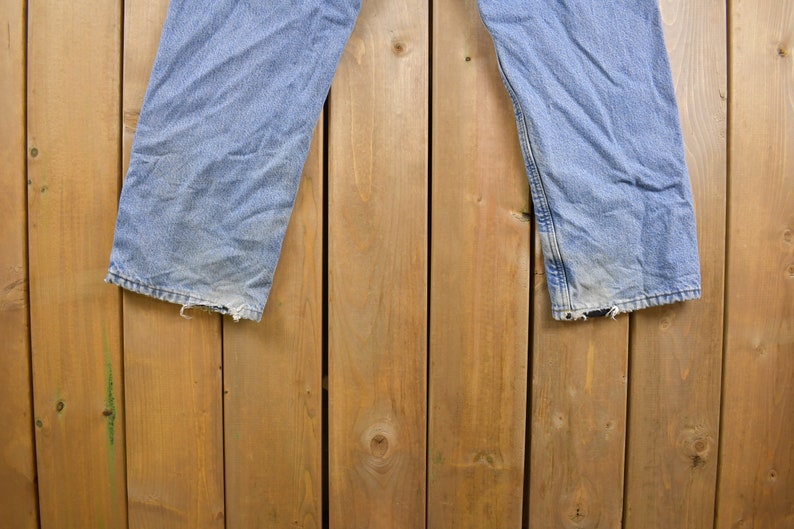 May include: A pair of light blue denim jeans hanging on a wooden fence. The jeans have a faded look and are slightly distressed.