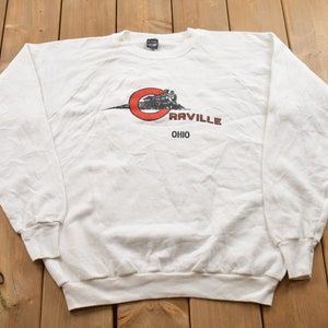 May include: White long-sleeved sweatshirt with a red circle and a black and white illustration of a train with the text "Carville Ohio" printed on the front.