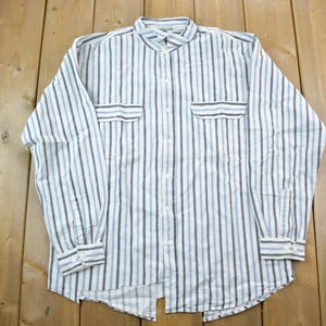 May include: A white long-sleeved button-down shirt with blue and brown vertical stripes. The shirt has two chest pockets and a mandarin collar.