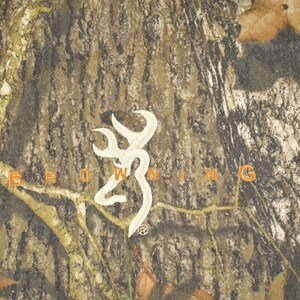 May include: Camouflage pattern with the word "BROWNING" in orange letters. A white emblem is centered above the word. The background has a mix of brown, green, and tan colours, with some leaves.