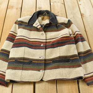Könnte beinhalten: Vintage Jacke mit Streifenmuster in Beige, Rot, Blau und Grün. Die Jacke hat einen schwarzen Kragen und zwei Vordertaschen. Sie ist zugeknöpft und scheint aus einer Wollmischung zu sein.