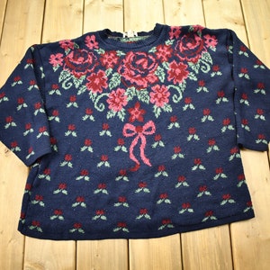 Può includere: Un maglione blu navy con un motivo floreale. Il maglione ha un collo rotondo e maniche lunghe. Il motivo floreale è in tonalità di rosa, rosso e verde.