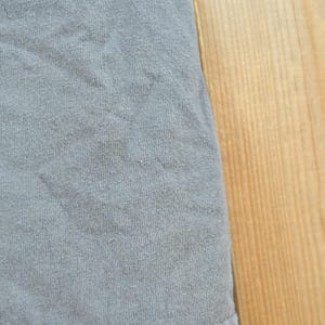 May include: Close-up of a section of a light blue fabric with a textured surface. The fabric is slightly wrinkled. The right side of the image shows a section of a light brown wooden surface.